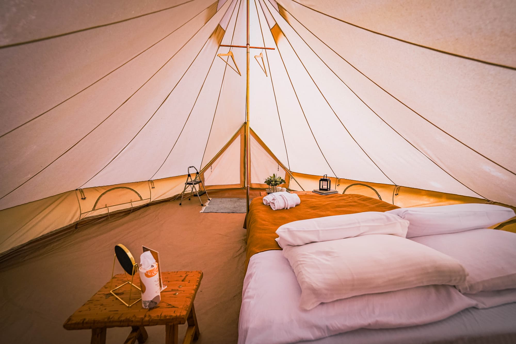 Inside a furnished glamping bell tent — queen bed, robes, lantern and layered rugs